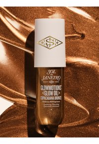 Flacon de Sol de Janeiro Glowmotions Glow Oil en teinte Copacabana Bronze sur un fond scintillant bronze.