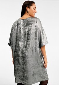 Metallisch silbernes Kleid mit lässiger Passform, kurzen Ärmeln und einem Reißverschluss im Rücken. Weicher Stoff mit unregelmäßigem Glanz und geschwungener Saumlinie.