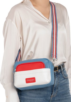 Woman wearing a crossbody bag with blue, white, and red color blocks and a striped red, white, and blue adjustable shoulder strap.