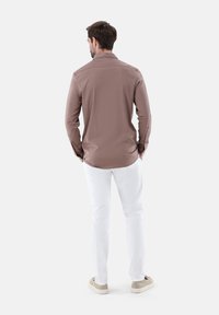 Hellbraunes, langärmliges Hemd mit schlichtem Design, ausgestattet mit einem Kragen und slim fit, kombiniert mit weißen Hosen und hellbeigen Sneakern.