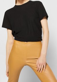 T-shirt en coton noir à manches courtes et col rond, associé à un pantalon en cuir moutarde taille haute, ajusté.