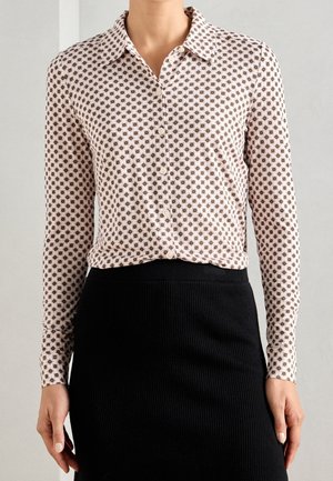 Femme portant un chemisier à manches longues boutonné et à motifs, rentré dans une jupe noire côtelée taille haute.