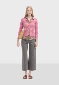 Lyserød strikket cardigan med horisontale striber, blomster-bluse, grå brede bukser og brune sandaler. Tilbehøret omfatter en vævet crossbody taske.