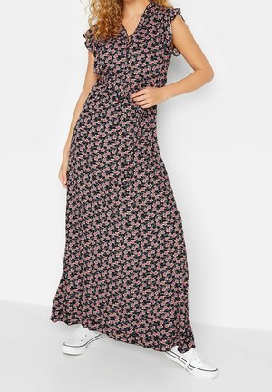 Robe longue fleurie noire avec des fleurs roses et blanches, manches à volants et encolure en V. Portée avec des baskets blanches. Texture de tissu lisse.