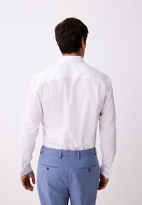 Vit långärmad skjorta med standardkrage och knäppta manschetter. Ljusblå kostymbyxor med två bakfickor och knappdetaljer.