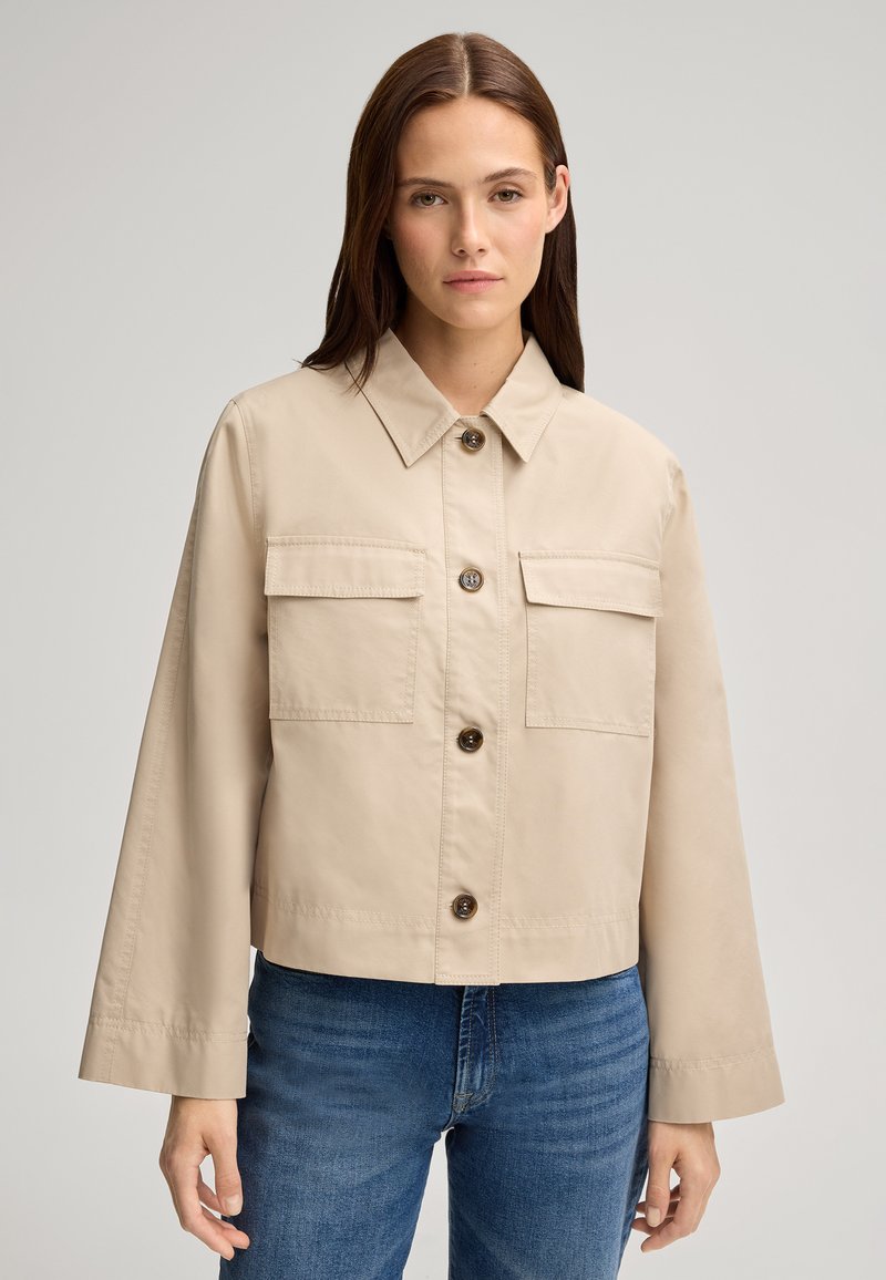 Giacca cropped beige con colletto, bottoni frontali e due tasche sul petto; realizzata in tessuto morbido con vestibilità rilassata.