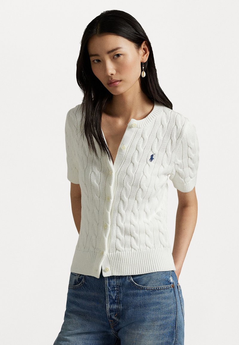 Cardigan blanc à manches courtes en tricot torsadé, présentant une fermeture à boutons sur le devant et un col rond, avec un petit logo bleu sur la poitrine.