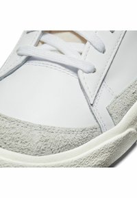 Witte sneaker met een gladleren bovenwerk en een gestructureerde grijze suède neuskap. Voorzien van witte veters en een gemêleerde rubberen zool.