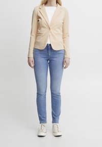 Světle broskvový elegantní blejzr s jedním knoflíkem a dvěma bočními kapsami, spárovaný se světle modrými skinny džíny a bílými teniskami.