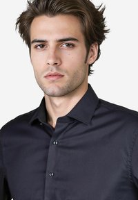 Zwarte overhemd met een gestructureerde kraag, voorzien van glanzende knopen en een gladde stoftextuur, gedragen door een model met kort, gestyled haar.