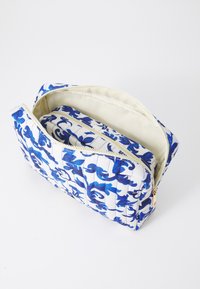 Quilted cosmetic bag with blue floral design on a white background. Features a zip closure and a smaller inner pouch. Smooth texture.