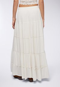 Gonna maxi bianca con design a strati, caratterizzata da sottili dettagli in pizzo e un tessuto fluido, che crea una texture morbida e una silhouette rilassata.