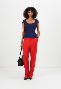 Haut peplum marin avec manches capes, associé à un pantalon rouge taille haute et des talons noirs pointus. Les accessoires comprennent un sac à main noir.