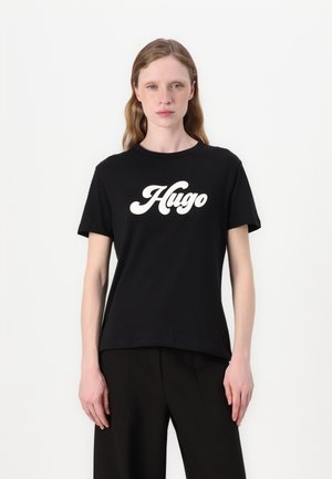 Černé bavlněné tričko s kulatým výstřihem. Má velké bílé logo "Hugo" v kurzívě. Krátké rukávy a volný střih.