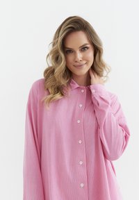 Różowa koszula w paski o luźnym kroju, z kołnierzykiem i zapięciem na guziki. Miękka tekstura z widocznymi pionowymi paskami i długimi rękawami.