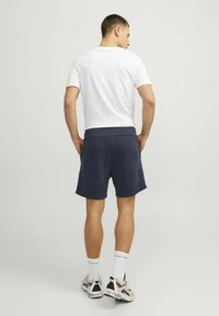 Marineblauwe sportshorts met een elastische tailleband, zijzakken en een textuurstof, gecombineerd met een eenvoudig wit T-shirt en sneakers.