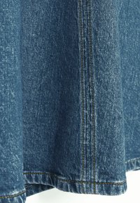Blauwe denim stof met een gestructureerd oppervlak, met contrasterende oranje stiksels langs de zoom en de zijnaad.