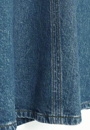 Blå denimstof med en tekstureret overflade, der har kontrastfarvet orange syninger langs kanten og sidesømmen.