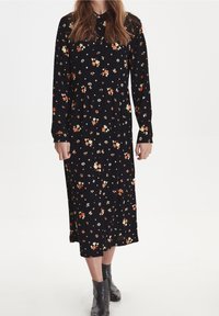 Abito nero a maniche lunghe con stampe floreali multicolori, vita arricciata e colletto. Il tessuto sembra morbido con una finitura liscia.