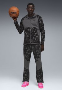Basketball outfit bestående af en grå hættetrøje med lynlås og dødningehovede accentuerende detaljer samt matchende bukser, parret med lyserøde sneakers.