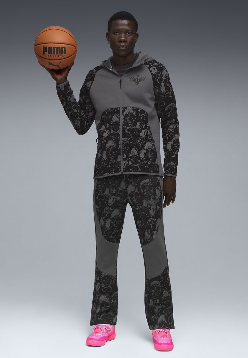 Tenue de basketball composée d'un sweat à capuche zippé gris avec des accents de motif crâne et un pantalon assorti, associé à des baskets rose vif.