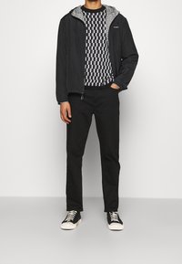 Svart lättviktsjacka med mönstrad huva, rutigt svart och vitt tröja, svarta byxor och svarta sneakers med vita sulor.