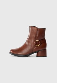 Brune lær ankle boot med rund tå, middels høy blokkhelt, og gull sirkelformet detaljer på siden. Glatt tekstur.