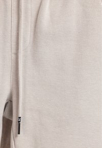 Lichtbeige textielstof met een subtiel weefpatroon. Bevat een zwarte trekkoordaccent en een zilveren metalen punt. Geschikt voor casual kleding.