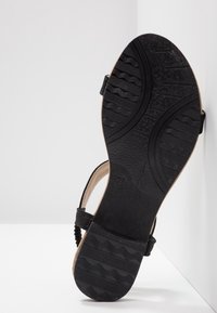 Semelle noire de sandale avec motifs de bande de roulement texturés, taille 37 visible, et bride de cheville sur un fond blanc en coin.