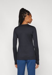 Long-sleeve black top with a rounded neckline, fitted design, and seam detailing. Worn with blue pants, showcasing a smooth, stretchy fabric.