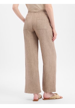 Person trägt beige weite Leinenhose mit aufgesetzten Taschen, kombiniert mit beigen Schlupfsandalen vor weißem Hintergrund.