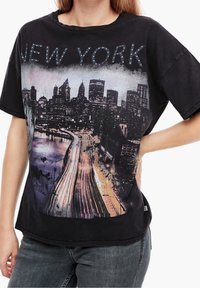 Mujer con una camiseta negra que tiene impresa la silueta del skyline de Nueva York y estelas de luz en una carretera por la noche.