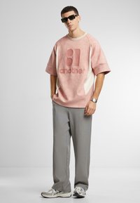Pink oversized sweatshirt with raised logo, cream side panels. Grey tailored trousers, white and silver sneakers with mesh detailing.