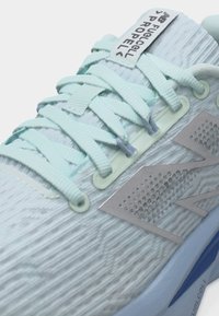 Κοντινή εικόνα φωτεινού μπλε παπουτσιού για τρέξιμο New Balance με υφή από πλέγμα στο πάνω μέρος, επίπεδα κορδόνια και ετικέτα «FuelCell Propel» στη γλώσσα.