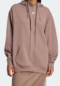 Överdimensionerad hoodie i mauve med en känguruficka, ribbade ärmslut och en liten vit Adidas-logotyp på bröstet. Mjuk tygstruktur.