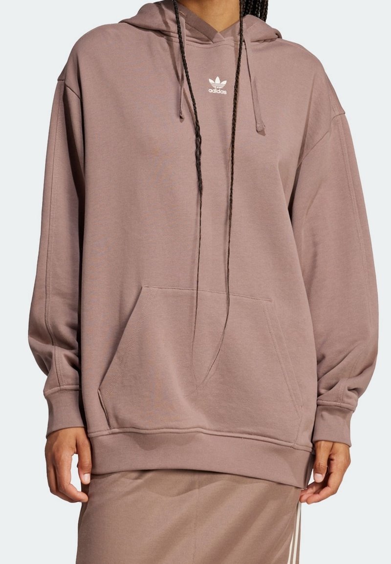 Överdimensionerad hoodie i mauve med en känguruficka, ribbade ärmslut och en liten vit Adidas-logotyp på bröstet. Mjuk tygstruktur.