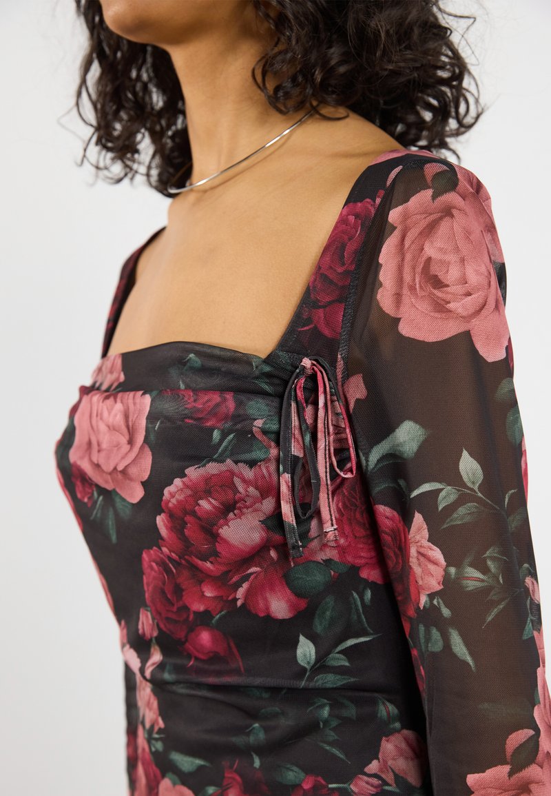 Vestido negro con flores que presenta grandes rosas en tonos rosa y rojo. Material transparente con un escote cuadrado y detalle de lazo en el lateral. Mangas largas.