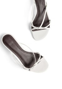 Vita klacksandaler med korsade remmar, en slät läderovandel och en kontrasterande mörkbrun innersula. Enkel, modern design.