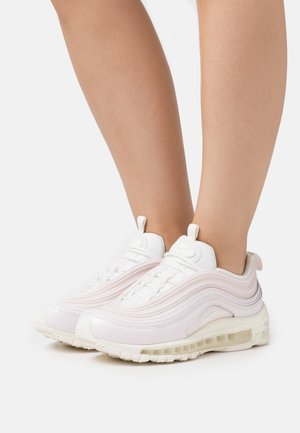 Weiße und hellrosa Sportschuhe mit sichtbarer Luftdämpfung, barfuß getragen vor schlichtem weißem Hintergrund.