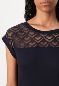 Marinblus med kort ärm som har ett genomskinligt, mönstrat meshparti med hjärtmotiv, kontrasterande texturer och rund halsringning.