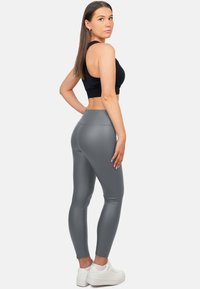 Leggings grigi alti in vita, realizzati in materiale elasticizzato e lucido, con un design aderente, abbinati a un top nero corto e sneaker bianche.
