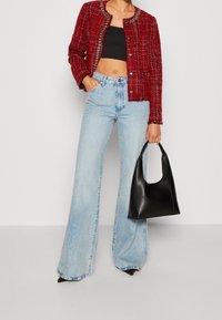 Vrouw in een rode tweed jas, zwarte crop top, lichtblauwe wijde spijkerbroek, zwarte puntige schoenen, met een zwarte leren handtas.