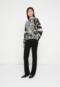 Schwarz-weiß gestrickter Pullover mit Tiger- und abstrakten Mustern, Rundhalsausschnitt, überschnittene Schultern, kombiniert mit schwarzen, eng anliegenden Hosen und High Heels.
