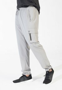 Light gray cargo pants with an elastic waistband, zippered side pocket, and spider logo on the thigh, paired with black athletic shoes.