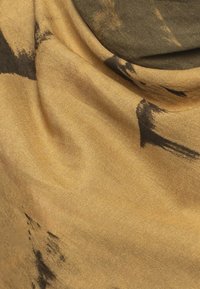 Tessuto marrone e oro con una superficie testurizzata presenta motivi astratti di pennellate nere, creando un effetto di drappeggio morbido.