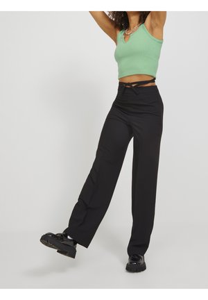 Pantaloni neri a gamba larga con una finitura liscia, dotati di una vita annodata, abbinati a un top a canottiera aderente verde menta. Scarpe nere chunky.