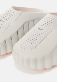 Λευκά παπούτσια από καουτσούκ με σχεδίαση slip-on, διάτρητο επάνω μέρος, στρογγυλεμένη μύτη και χοντρή, με ανάγλυφη υφή σόλα. Διαθέτουν μικρό ασημένιο λογότυπο ως διακοσμητικό στοιχείο.