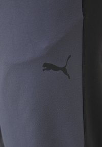 Marineblå atletiske bukser lavet af et glat materiale med et sort Puma-logo på siden, i en tætsiddende pasform og ankellængde design.