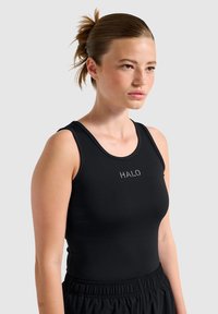 Zwarte mouwloze tanktop van rekbare stof, met een ronde halslijn en een subtiele "HALO"-logo aan de voorkant, gecombineerd met zwarte broek.