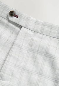 Tissu à carreaux gris clair avec un bouton marron foncé et une couture de boutonnière bordeaux sur la ceinture d'un vêtement.